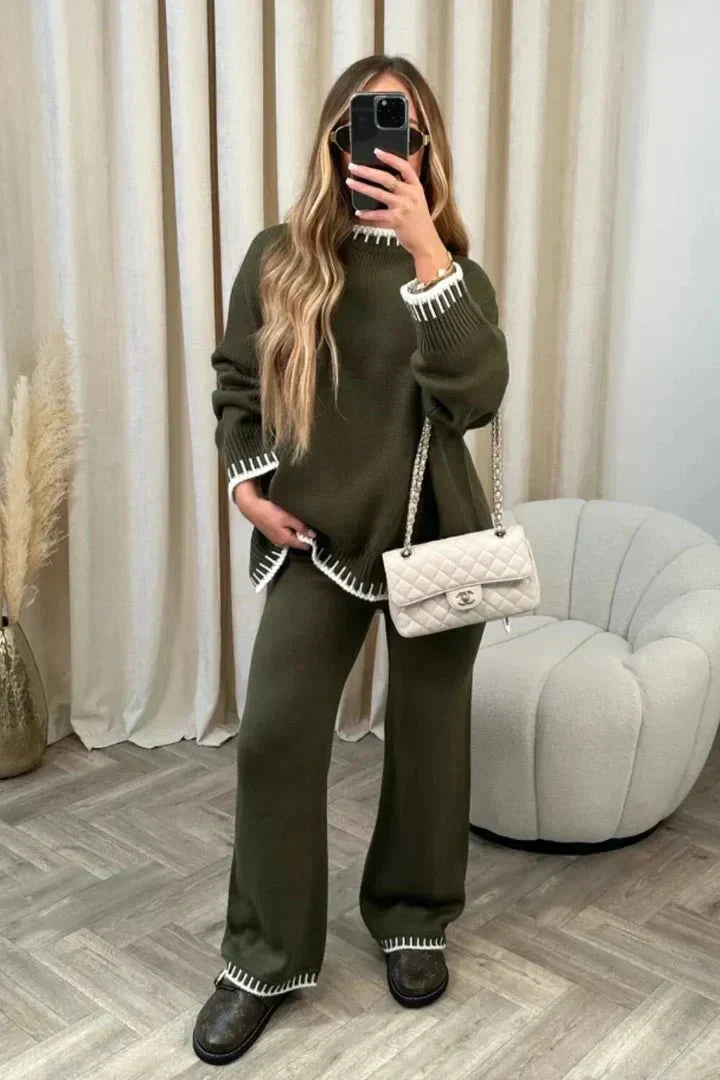 Woman taking a mirror selfie wearing a green outfit with white trim in a room with a gray chair and white curtains.