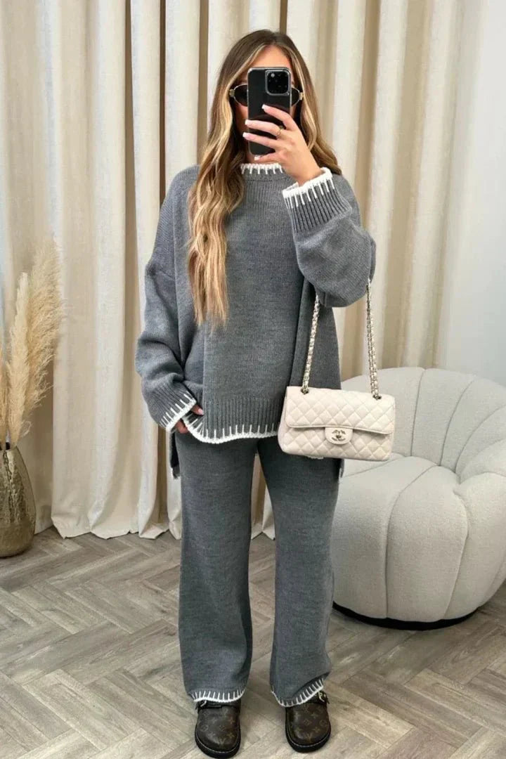 Person wearing a gray outfit with a white handbag in a room with curtains and a chair.