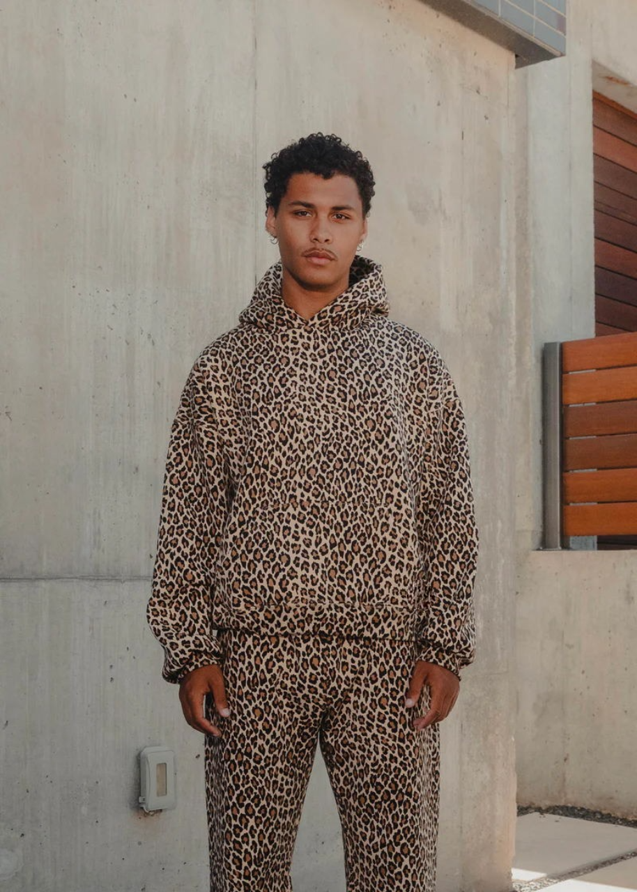 Person wearing a leopard print hoodie and pants standing against a concrete wall.