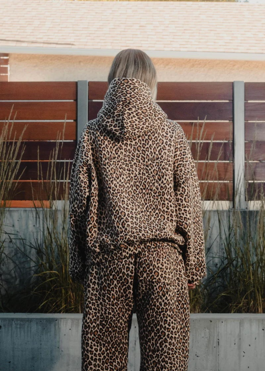 Person wearing a leopard print hoodie and pants standing in front of a modern building.
