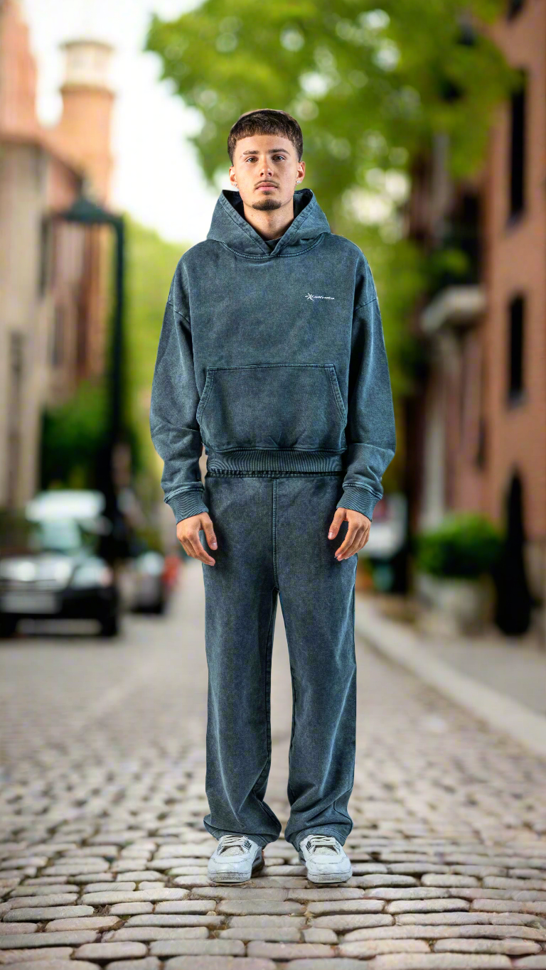 Man wearing a blue tracksuit standing on a street with buildings and trees in the background