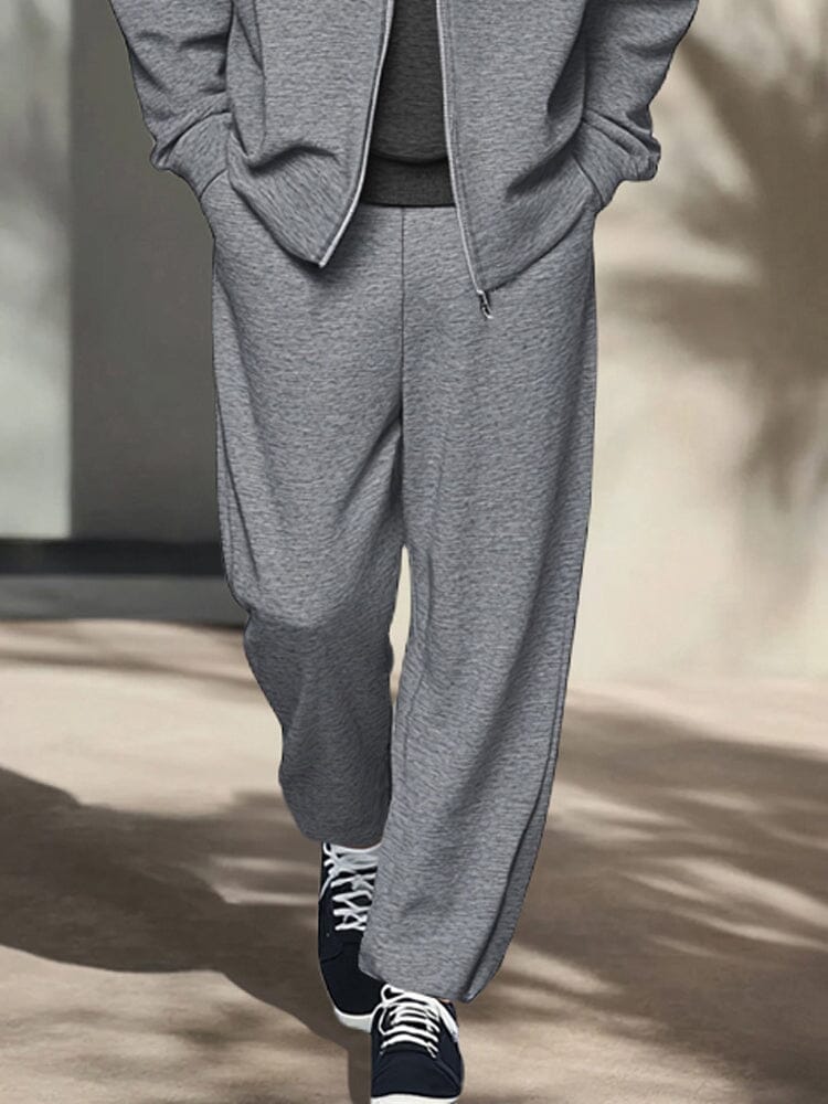 Person wearing a gray tracksuit with black sneakers on a neutral background
