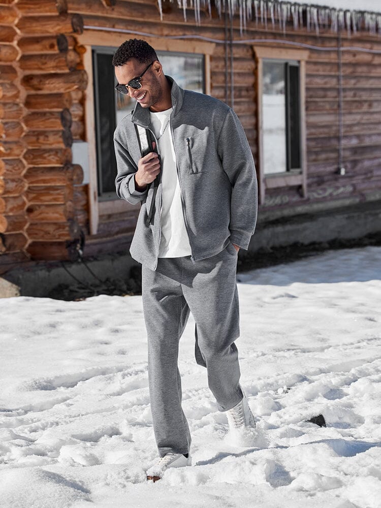 Man in gray tracksuit standing in snow near a wooden cabin
