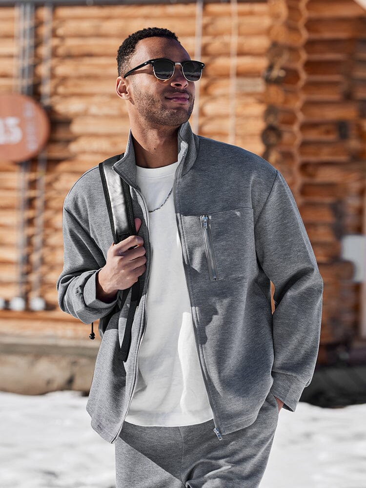 Man wearing a gray jacket and sunglasses standing in front of stacked logs.