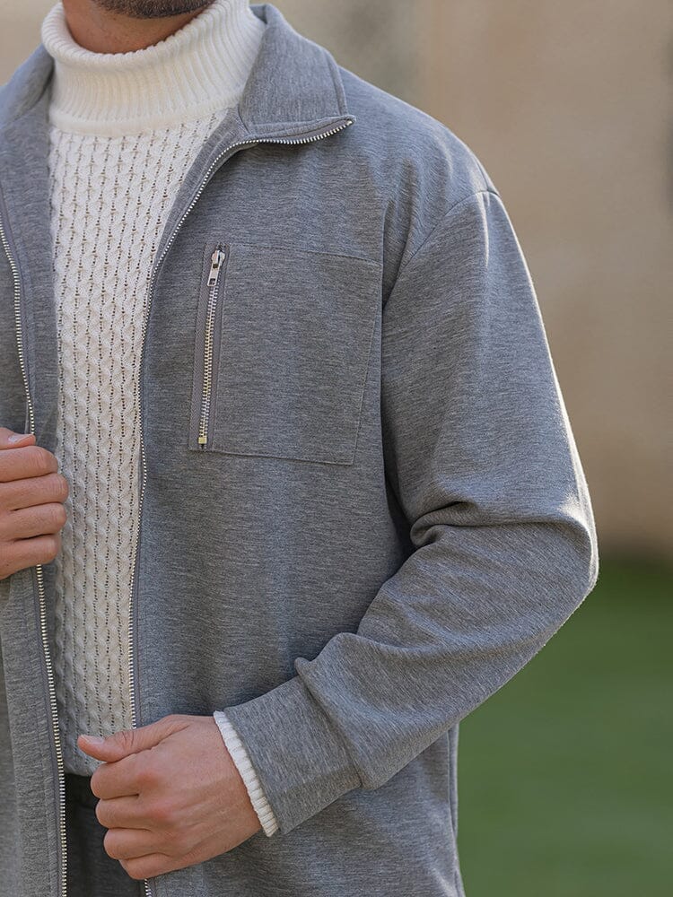 Gray zip-up jacket worn over a white turtleneck sweater with a blurred background