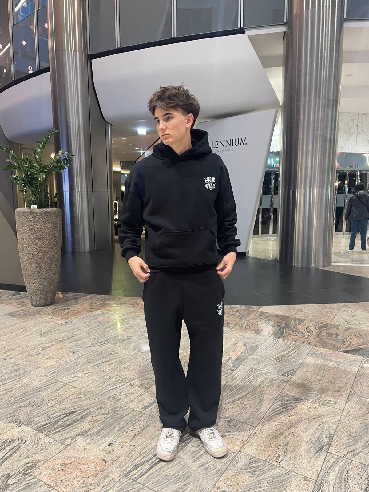 Person wearing a black hoodie and pants in a modern indoor setting