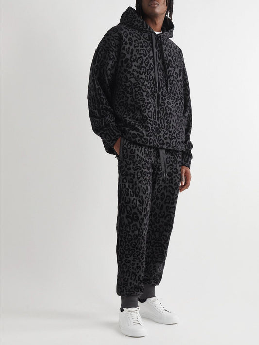 Person wearing a black leopard print tracksuit with white sneakers on a white background