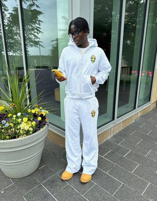 Person wearing a white tracksuit with a logo, standing outside a building.
