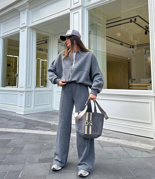 Person wearing a gray tracksuit with a cap, standing in front of a store.