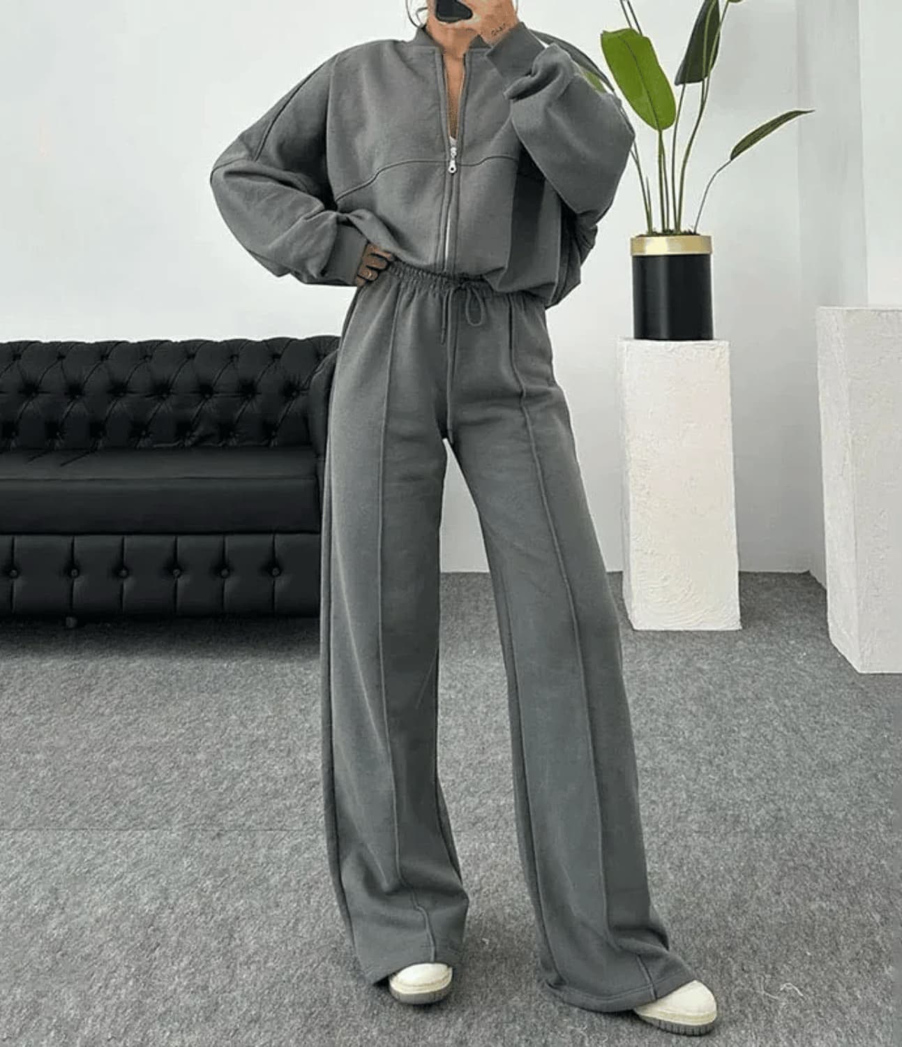 Person wearing a gray tracksuit in a room with a black sofa and white walls.
