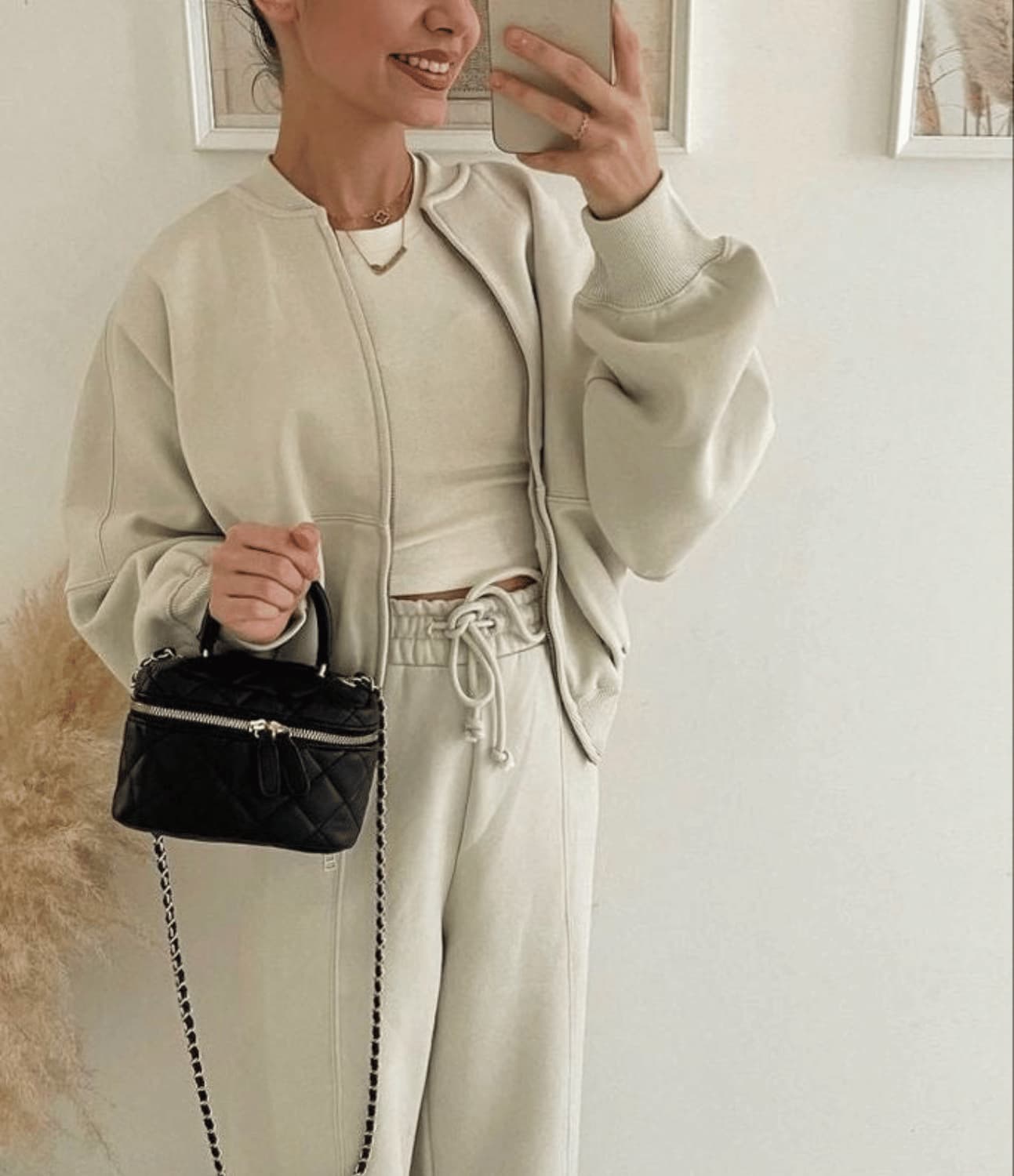 Person taking a mirror selfie wearing a beige outfit with a black handbag.