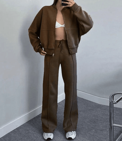 Person wearing a brown tracksuit with a white bralette against a plain wall.