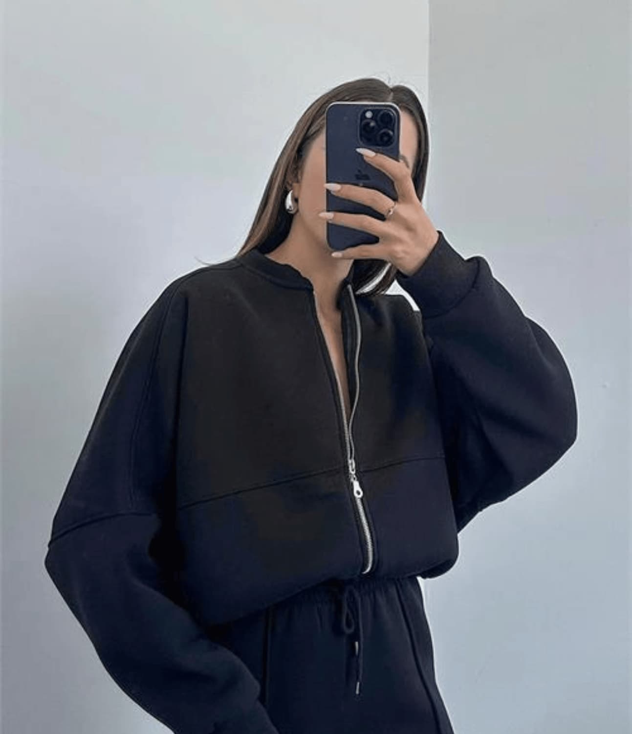 Person wearing a black zip-up hoodie and matching pants against a plain background