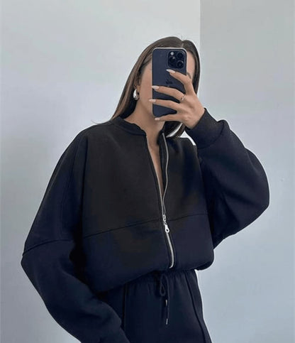 Person wearing a black zip-up hoodie and matching pants against a plain background