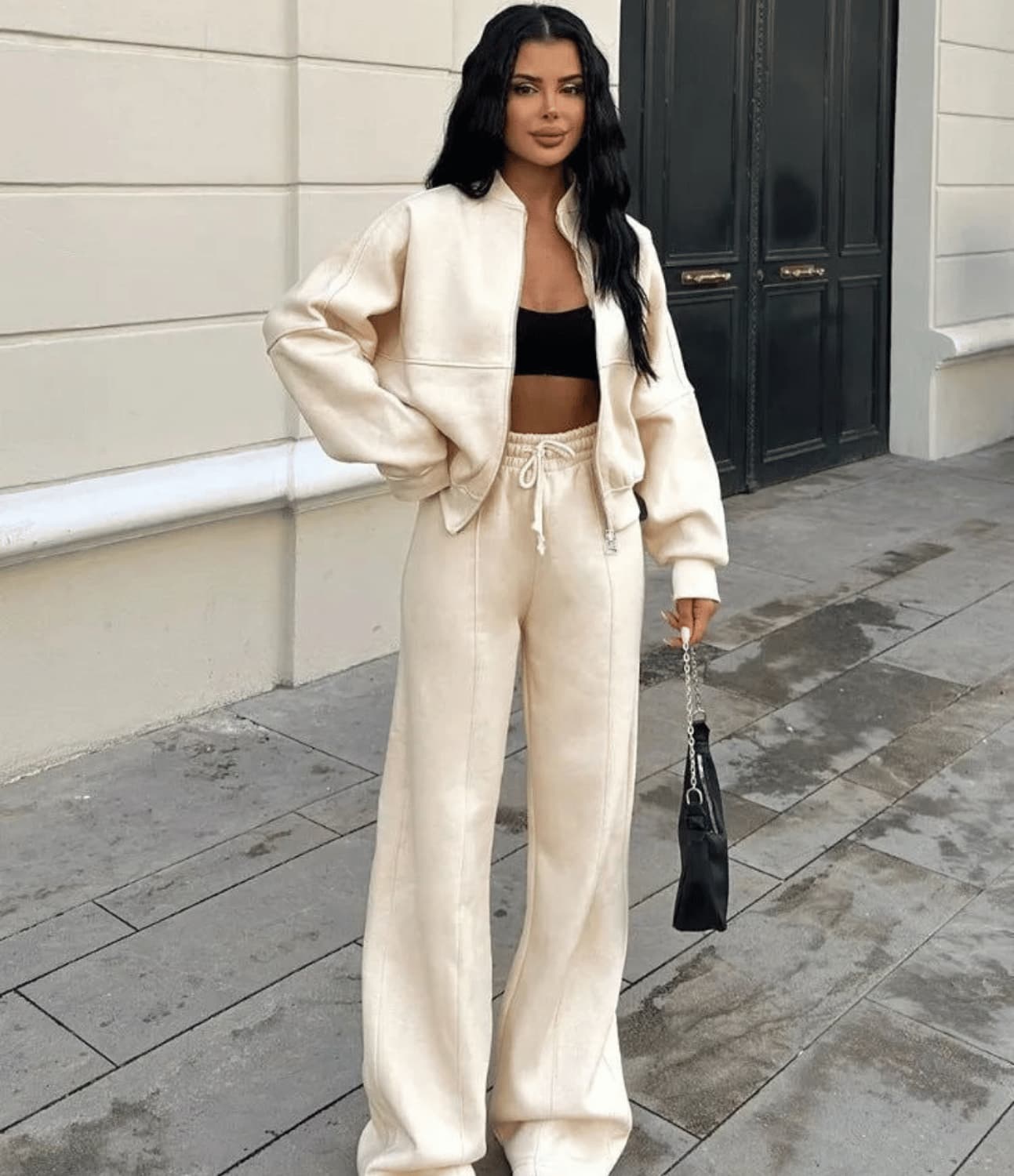 Woman in beige tracksuit holding a black handbag on a city street.