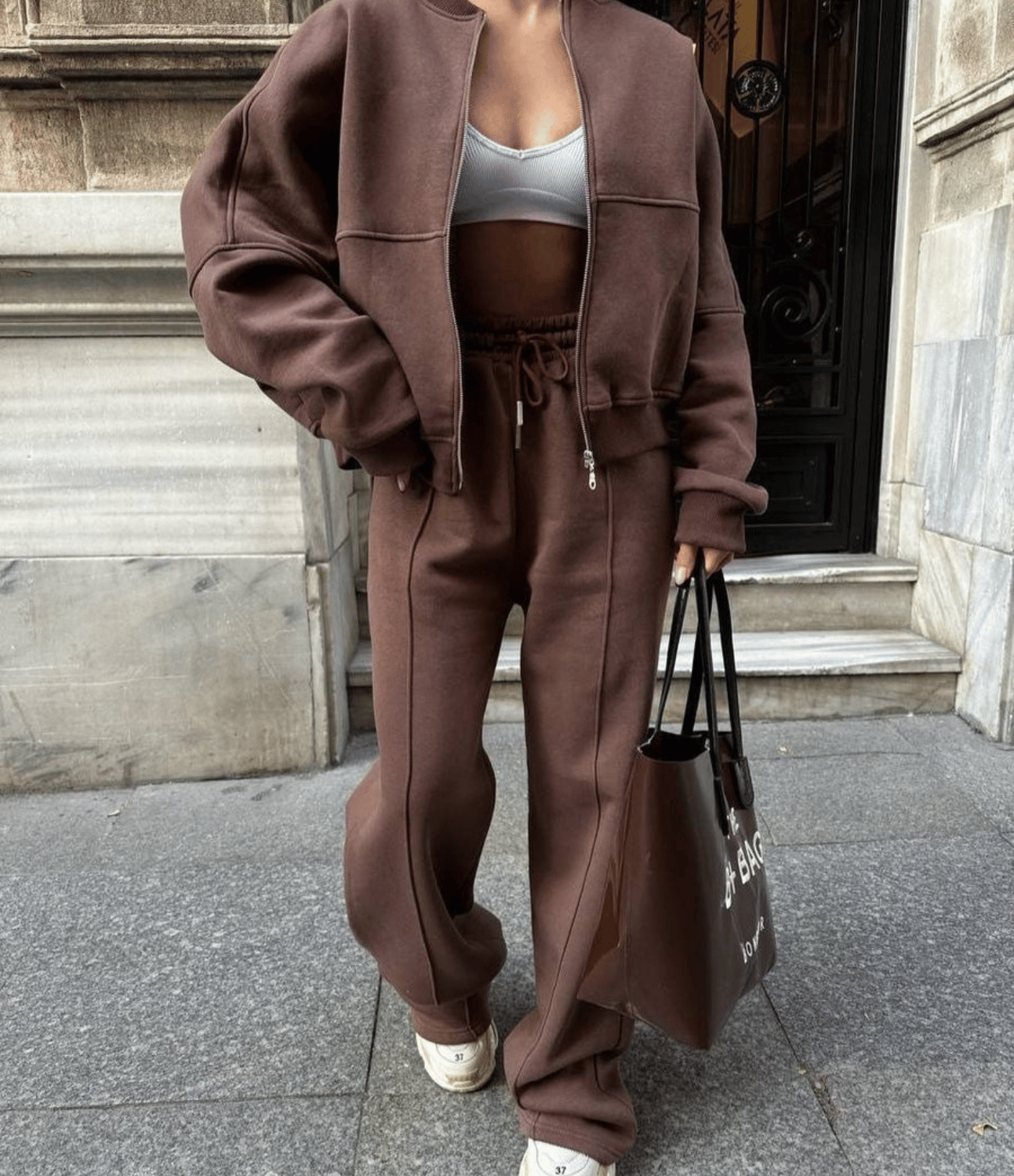 Person wearing a brown tracksuit holding a black bag on a city street.
