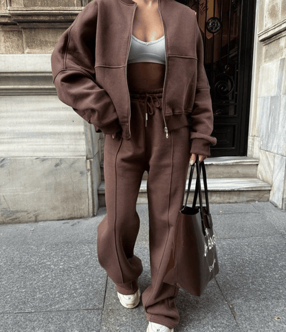 Person wearing a brown tracksuit holding a black bag on a city street.