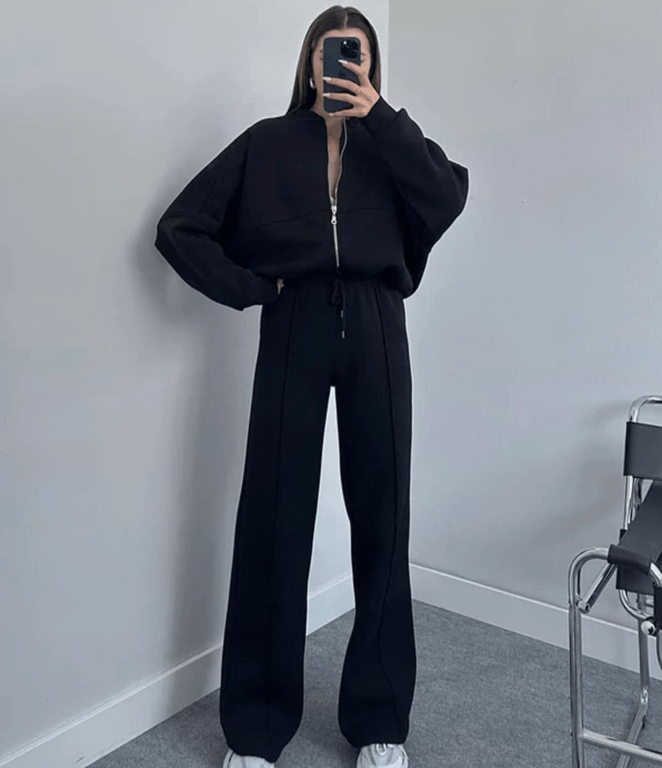 Person wearing a black outfit standing against a plain wall.