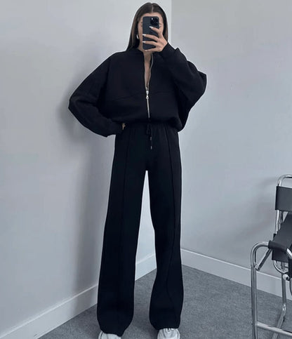 Person wearing a black outfit standing against a plain wall.