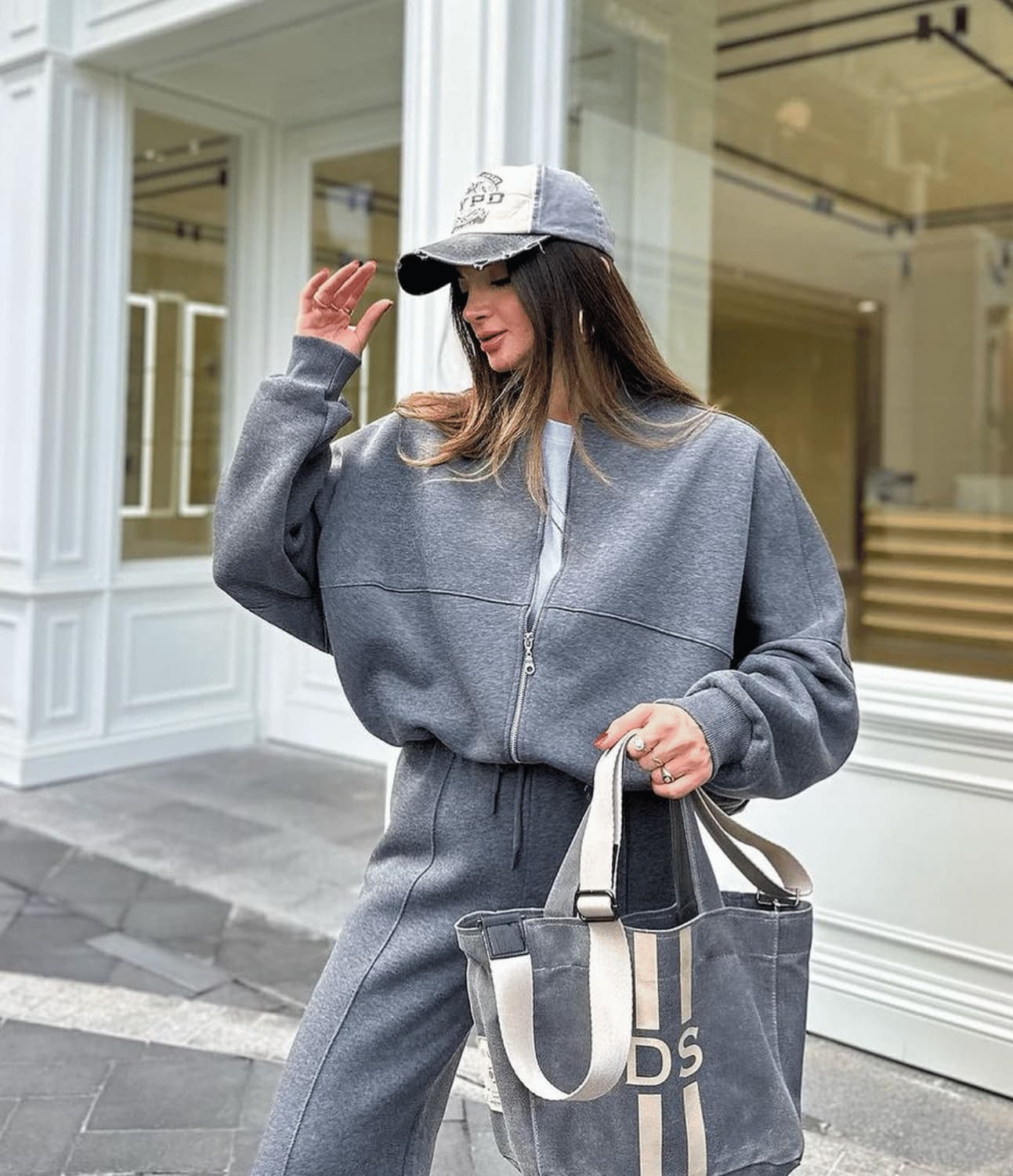 Woman in gray outfit with cap and tote bag walking on a street.