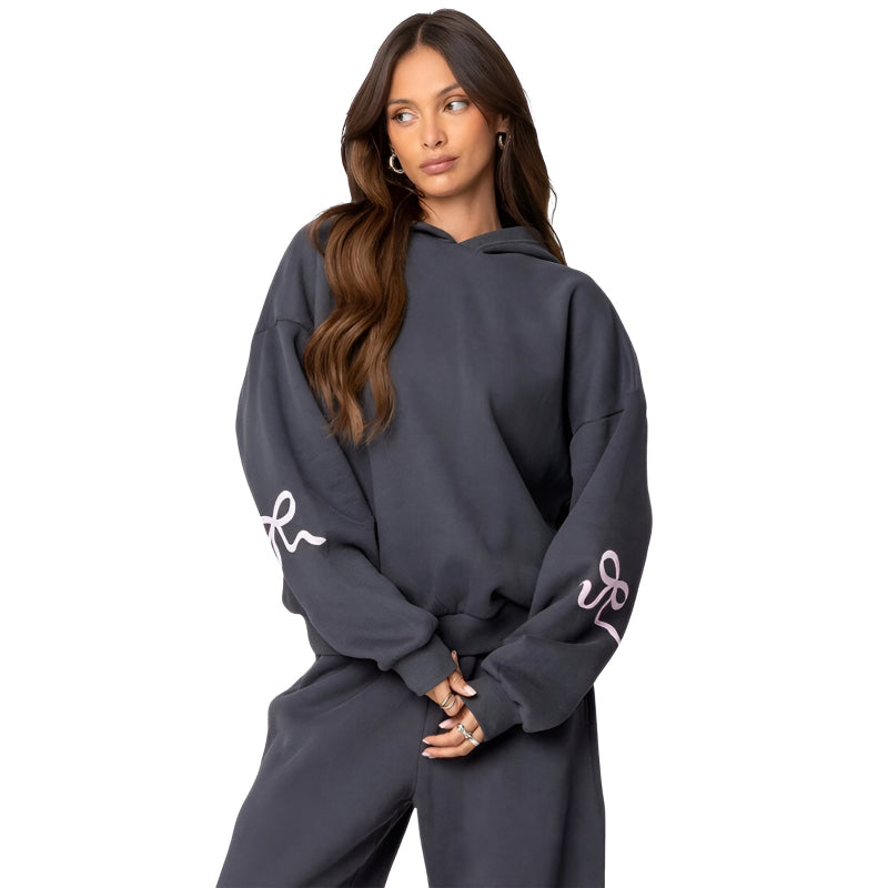 Woman wearing a dark gray hoodie and pants with white designs on a white background