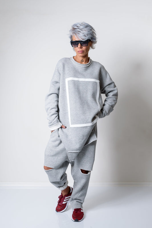 Person wearing a gray tracksuit with a white square design, red sneakers, and sunglasses on a white background