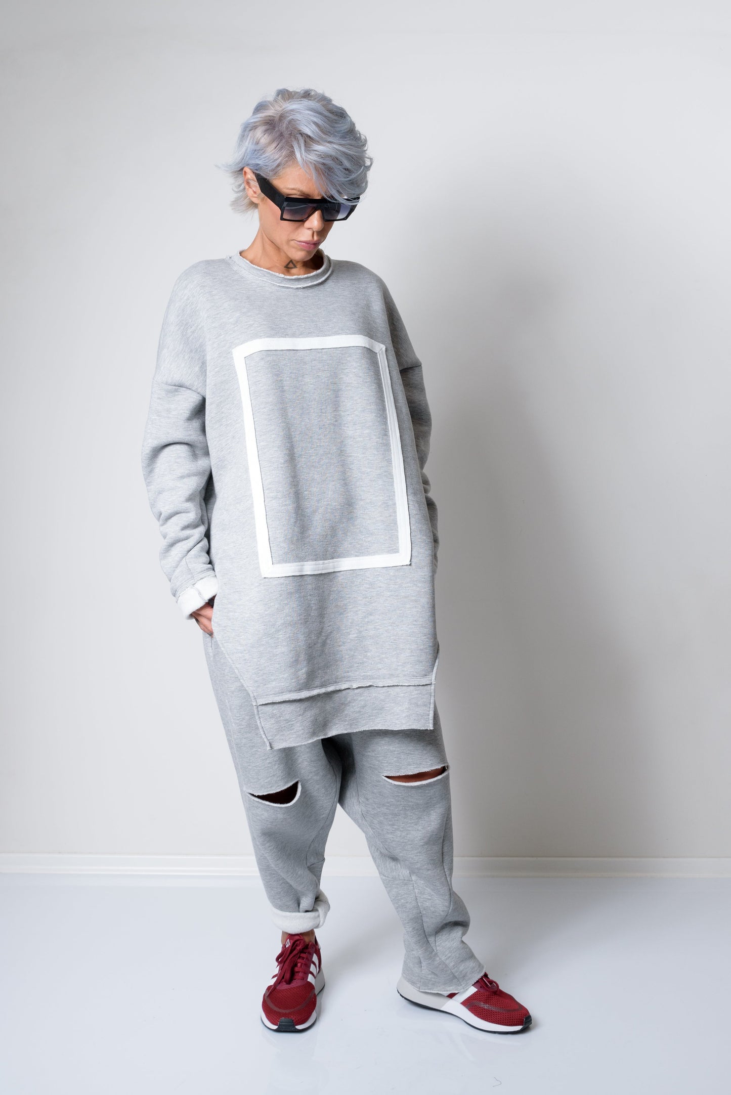 Person wearing a gray oversized sweater and pants with red shoes on a plain background