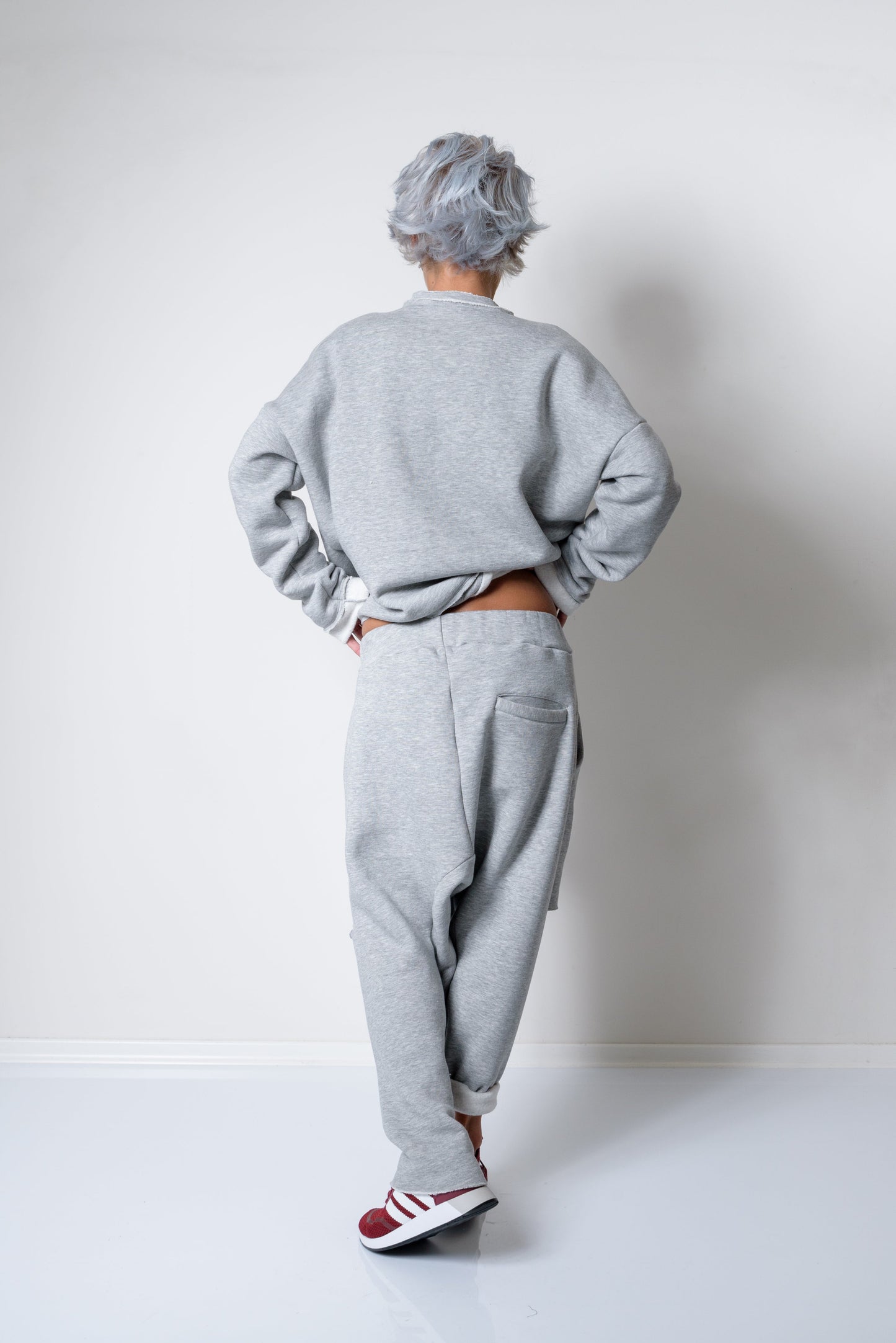 Person wearing a gray sweatshirt and pants standing against a white wall.