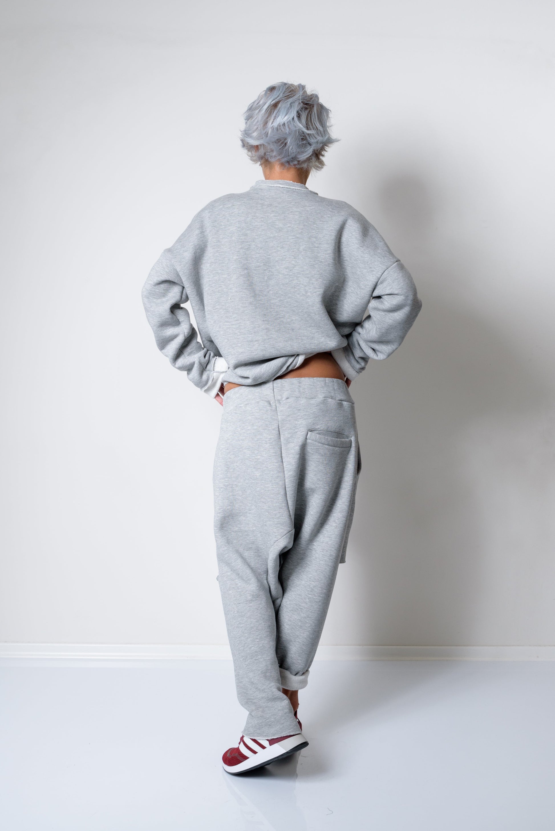 Person wearing a gray sweatshirt and pants standing against a white wall.
