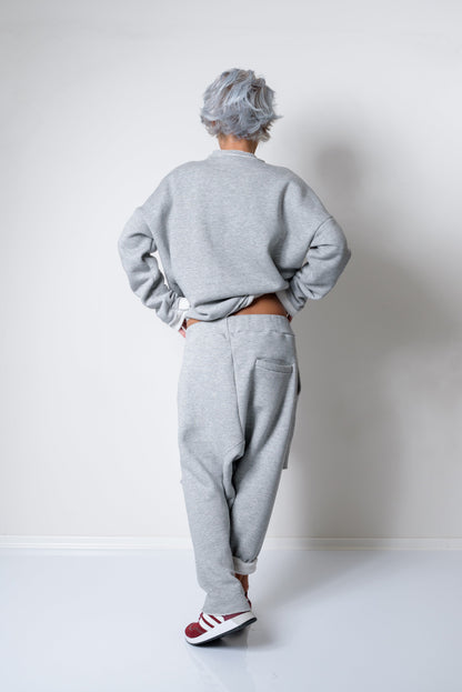 Person wearing a gray sweatshirt and pants standing against a white wall.