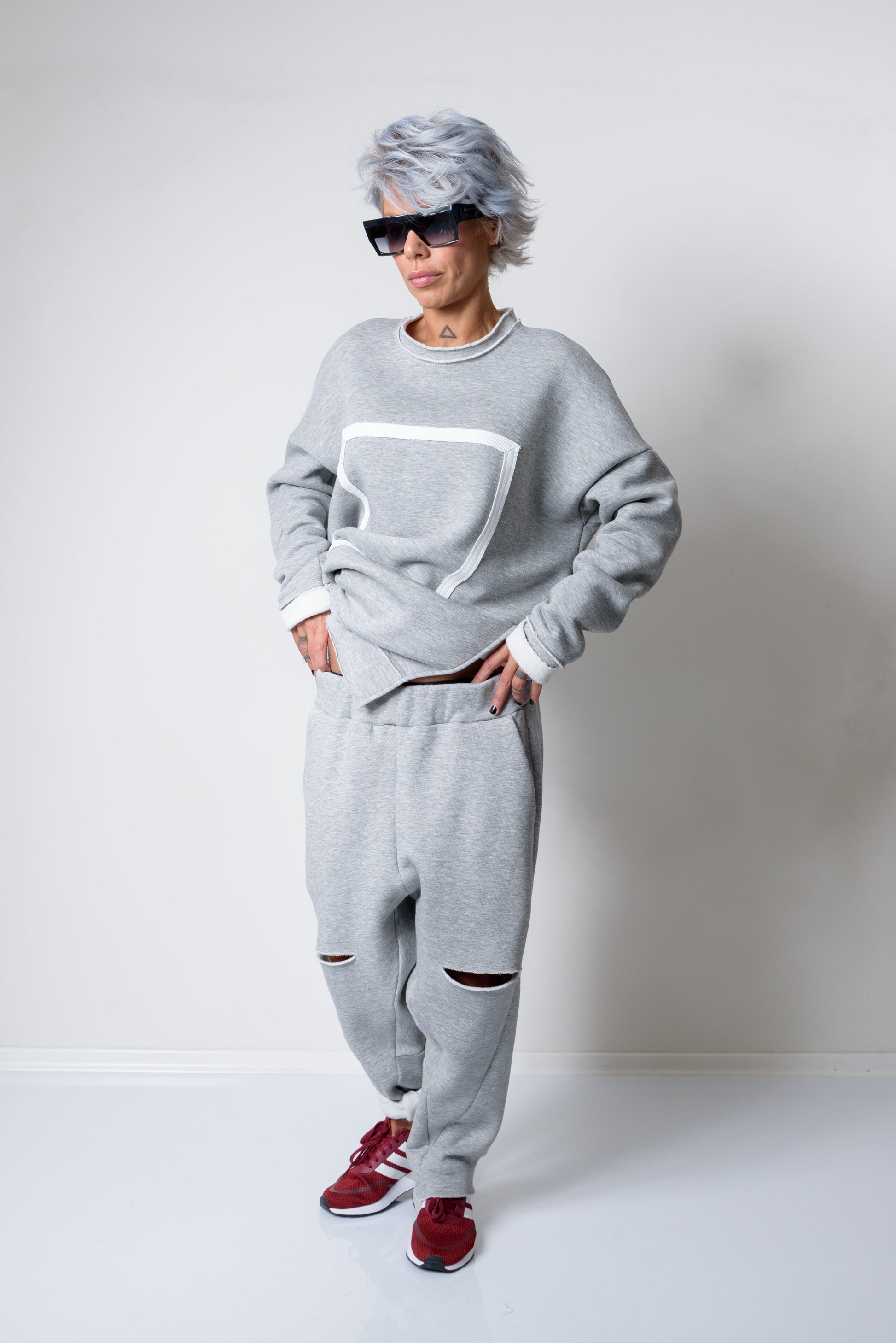 Person wearing a gray sweatshirt and pants with red shoes on a white background
