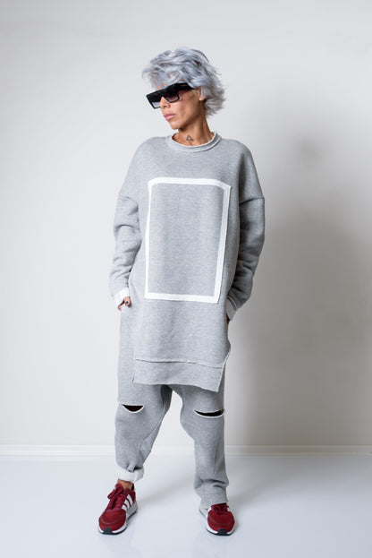 Person wearing a gray outfit with a large white square design on a plain background