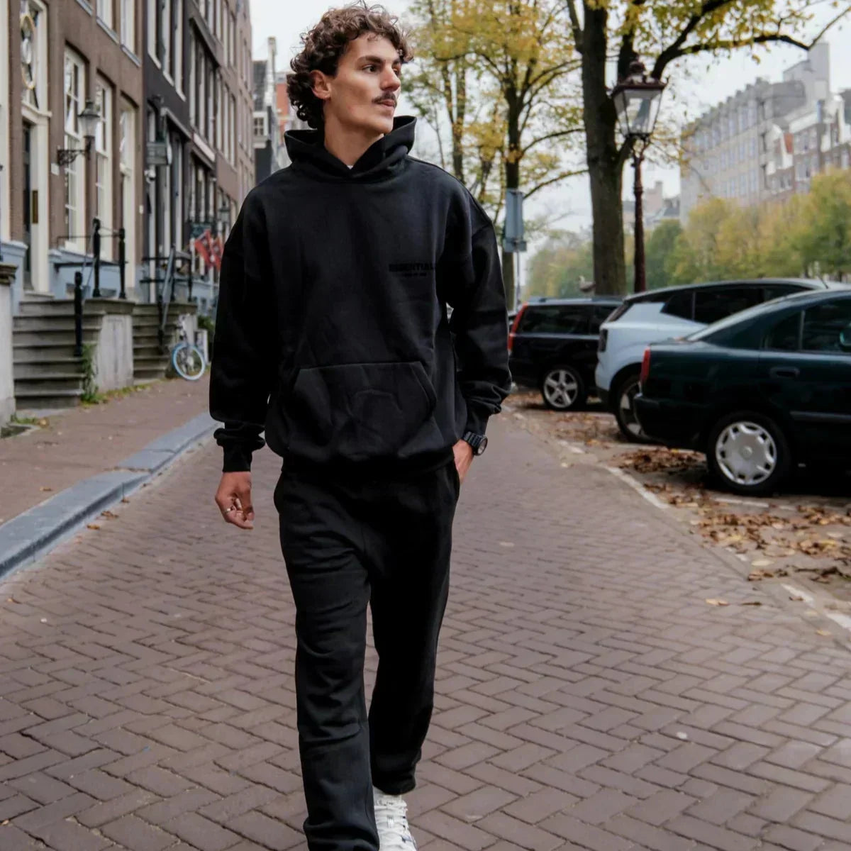 Man wearing a black hoodie and pants walking on a city street.