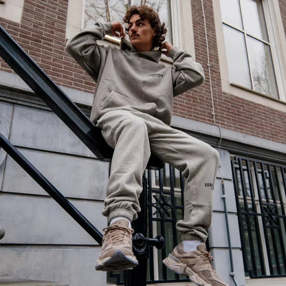 Person wearing a beige hoodie and pants sitting on a railing outdoors.