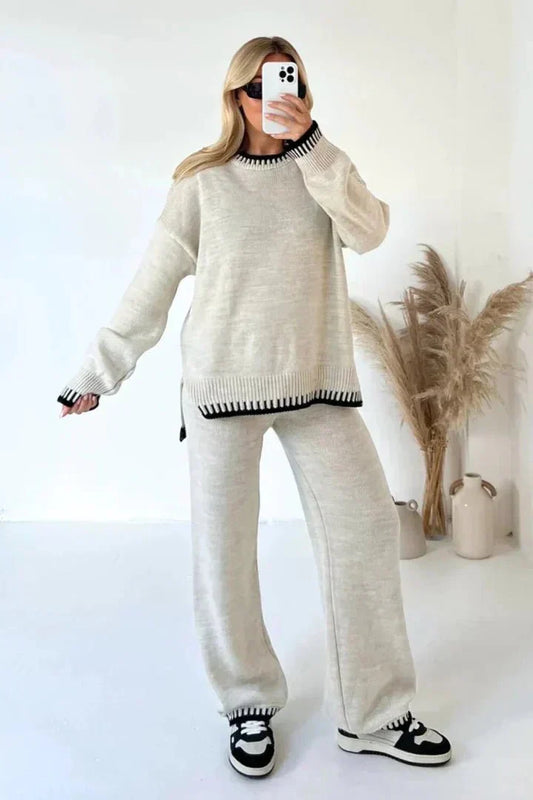 Person wearing a beige sweater and pants set with black accents, standing against a white background.