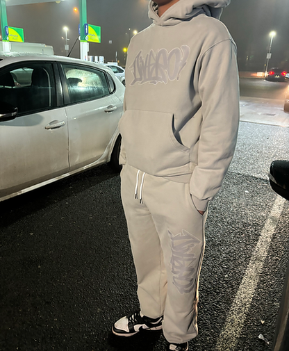 Person wearing a light gray hoodie and pants standing next to a car at night.