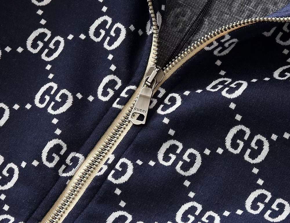 Close-up of a navy blue fabric with white 'GG' logo pattern and a gold zipper.