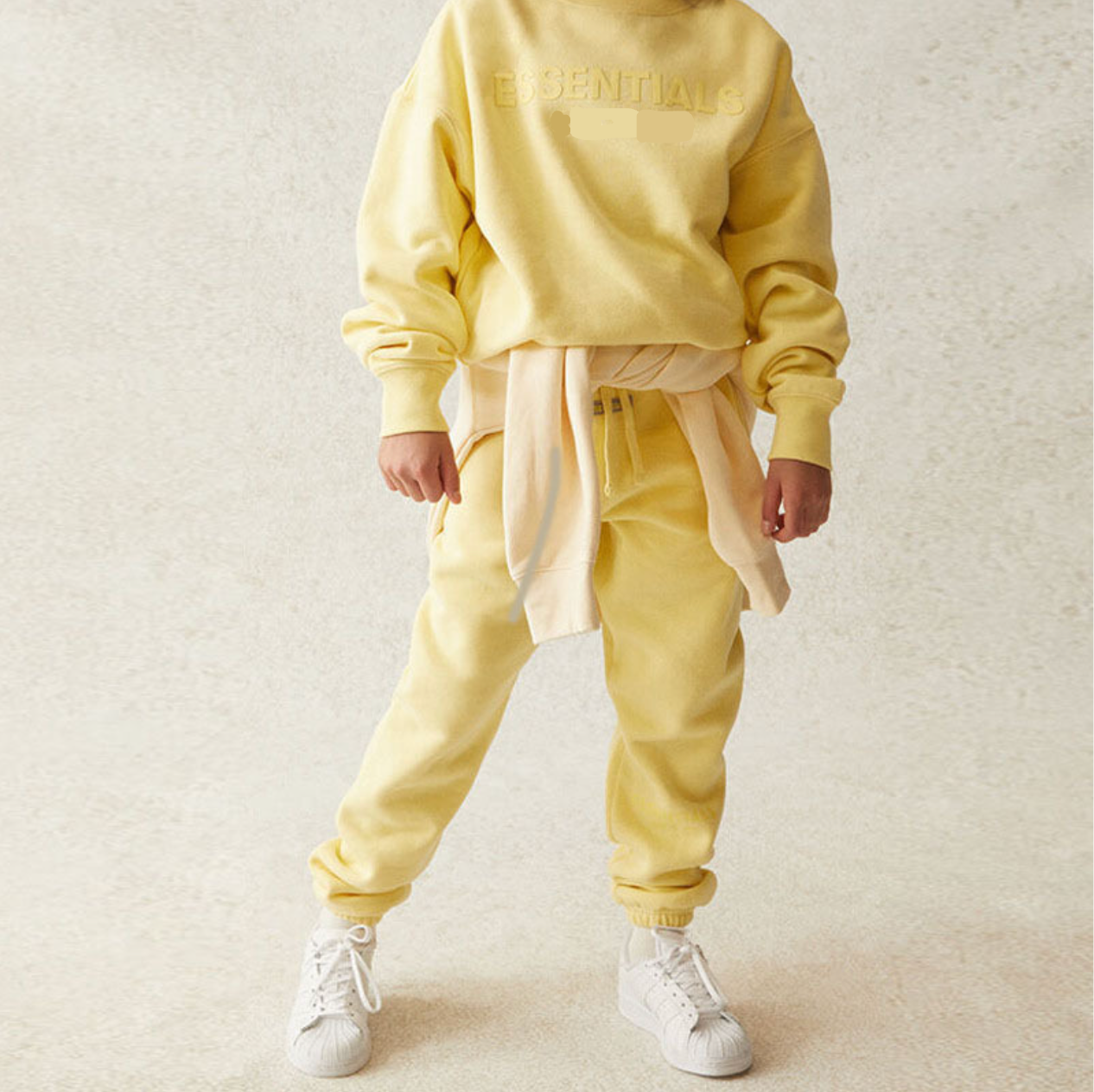 Person wearing a yellow tracksuit with white sneakers on a light background
