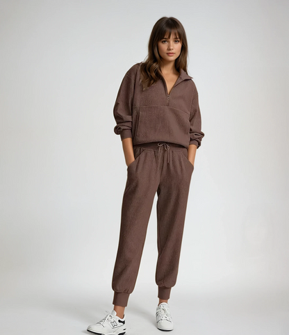 Woman wearing a brown tracksuit with white sneakers on a plain background