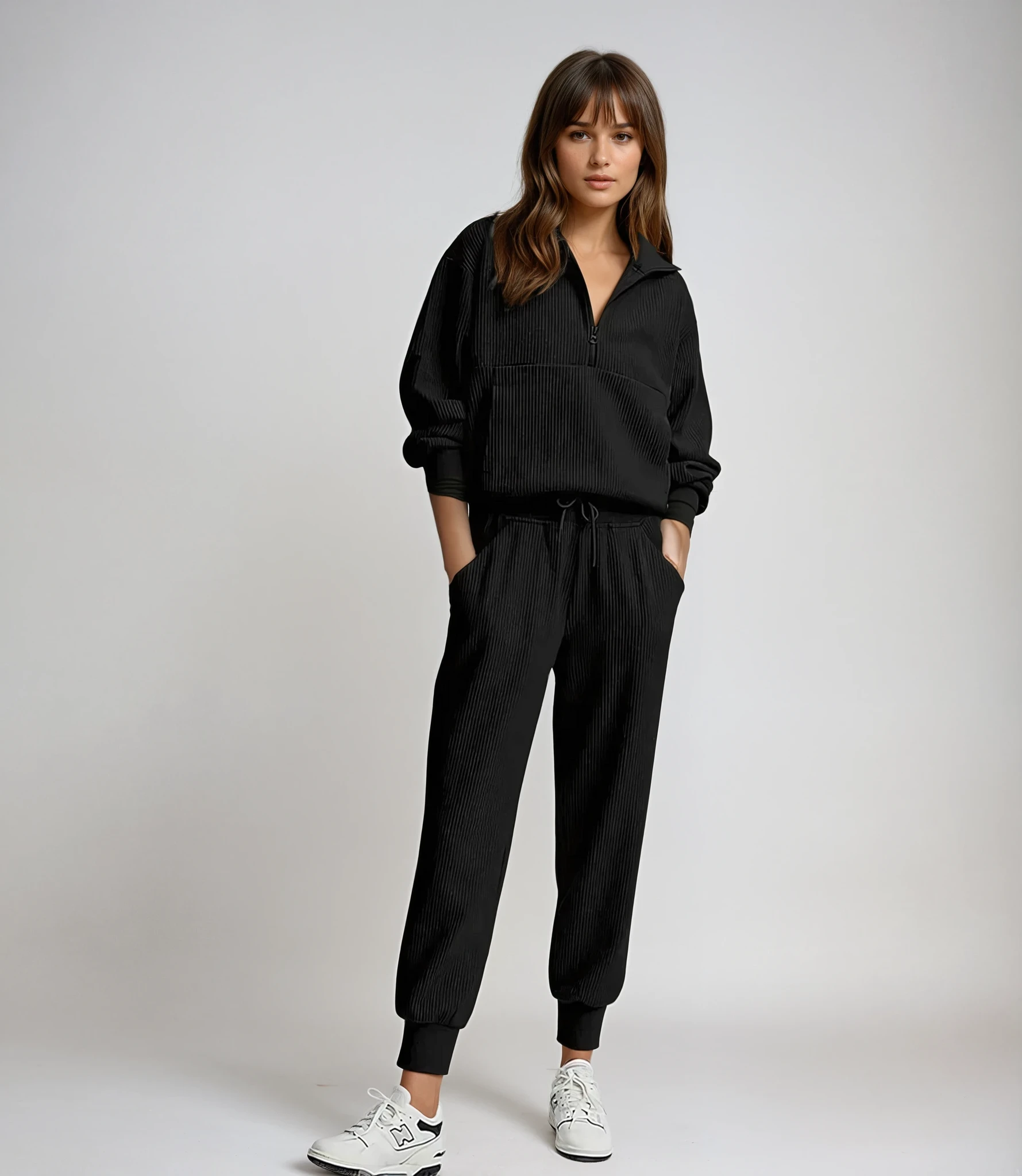 Woman wearing a black tracksuit with white sneakers on a plain background