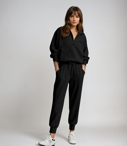 Woman wearing a black tracksuit with white sneakers on a plain background