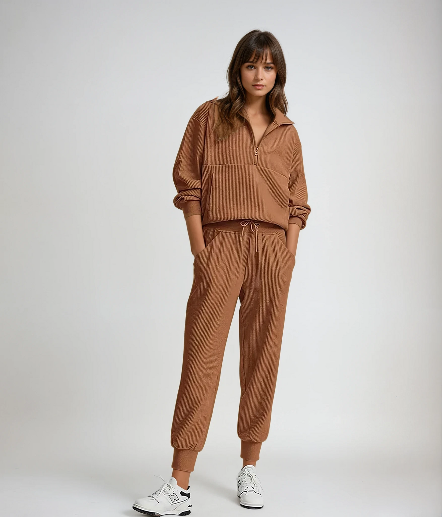 Woman wearing a brown tracksuit with white sneakers on a plain background