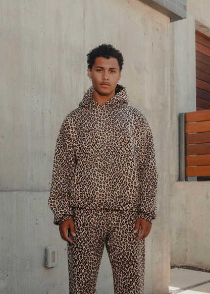 Person wearing a leopard print hoodie and pants standing against a concrete wall.