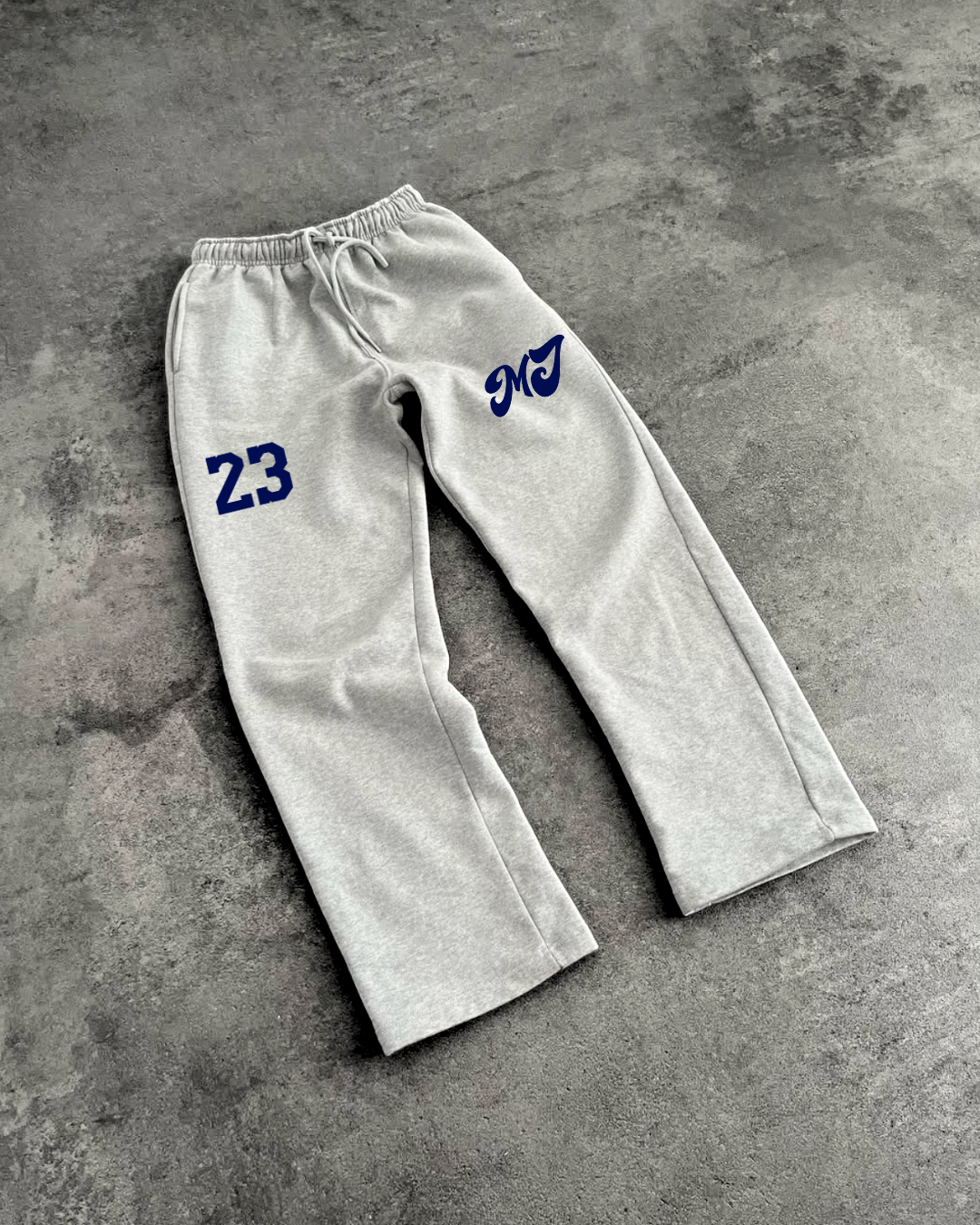 Gray sweatpants with blue numbering and lettering on a gray concrete surface