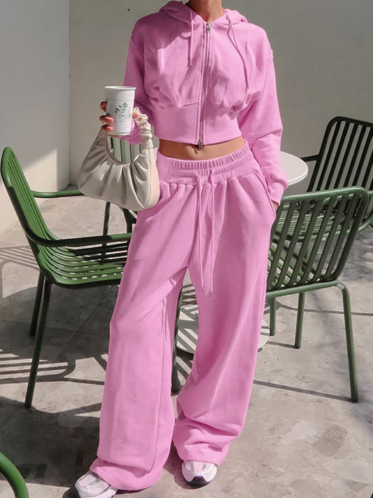 Person wearing a pink tracksuit holding a cup outdoors.