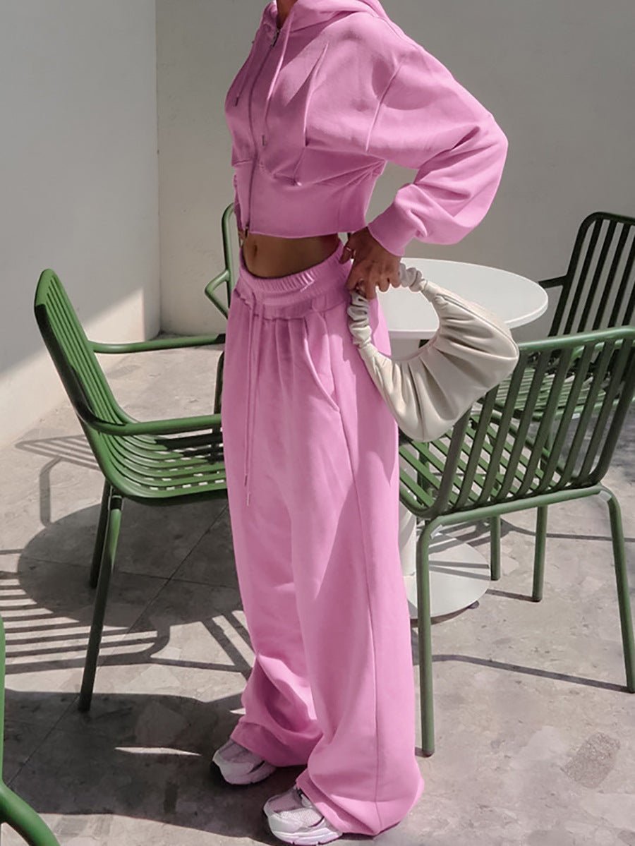Person wearing a pink outfit standing outdoors with green chairs and a white table in the background.
