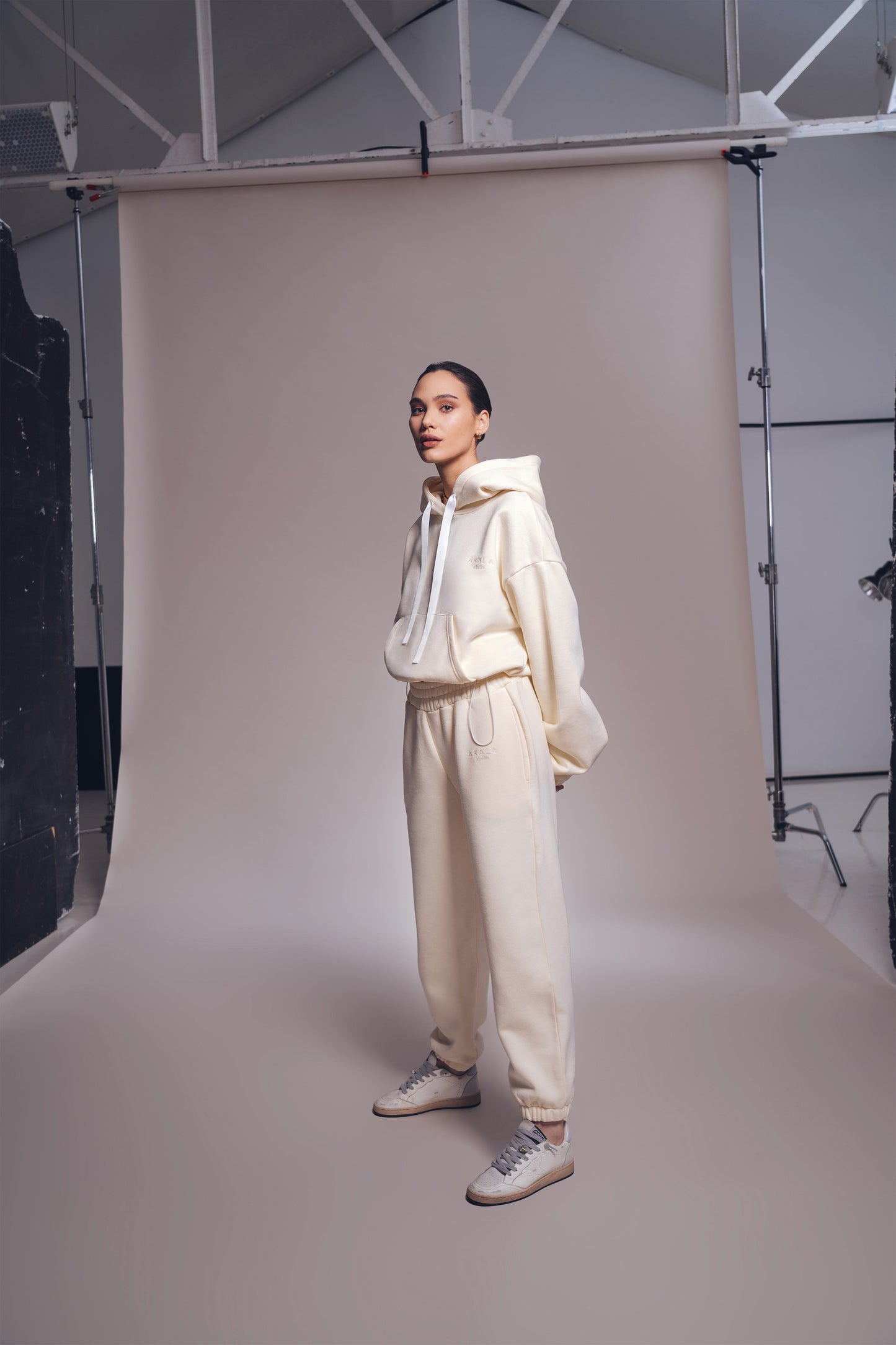 Person wearing a cream-colored outfit standing against a neutral backdrop in a studio setting