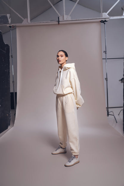 Person wearing a cream-colored outfit standing against a neutral backdrop in a studio setting