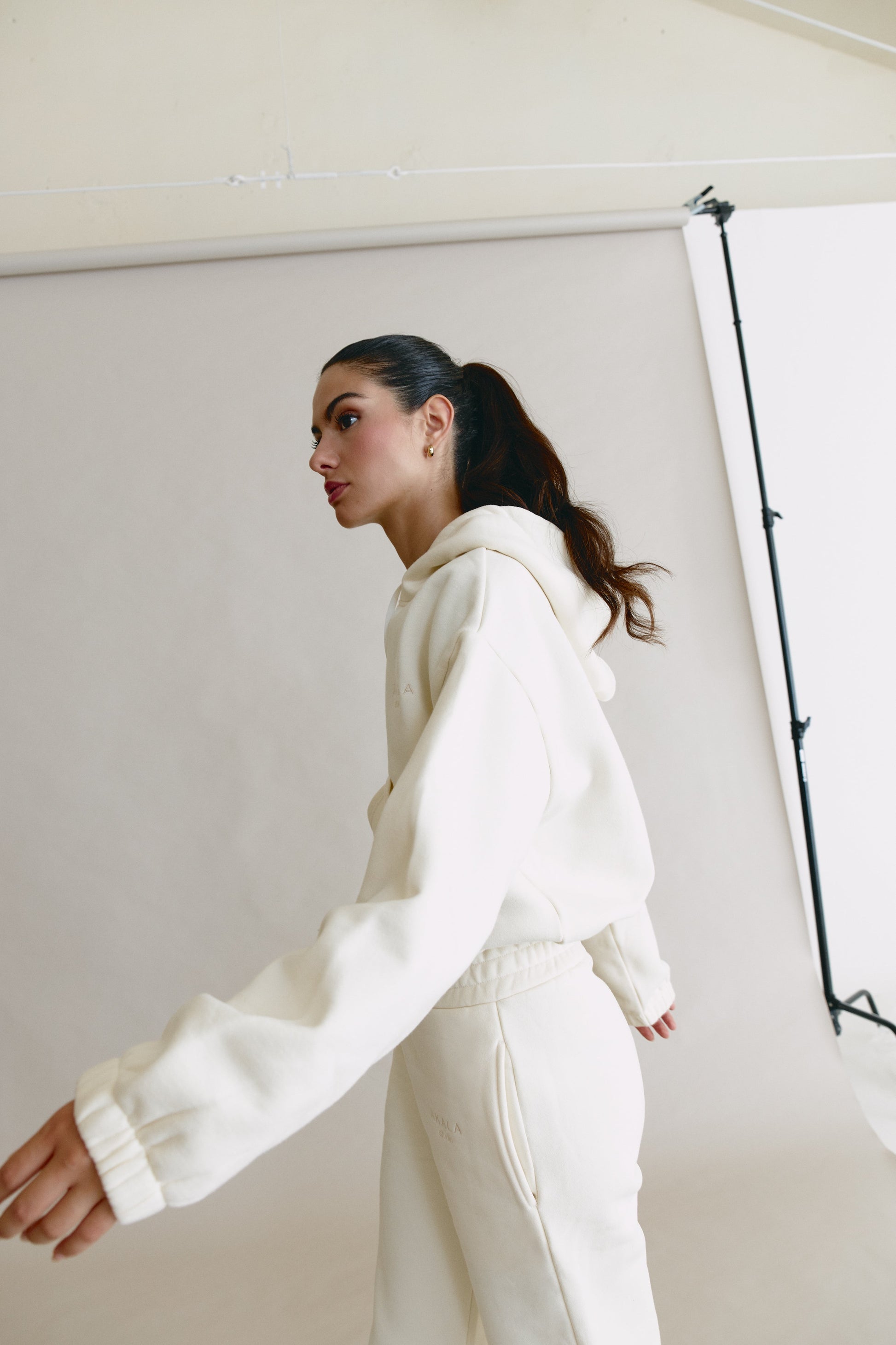 Person wearing a white hoodie and pants in a studio setting