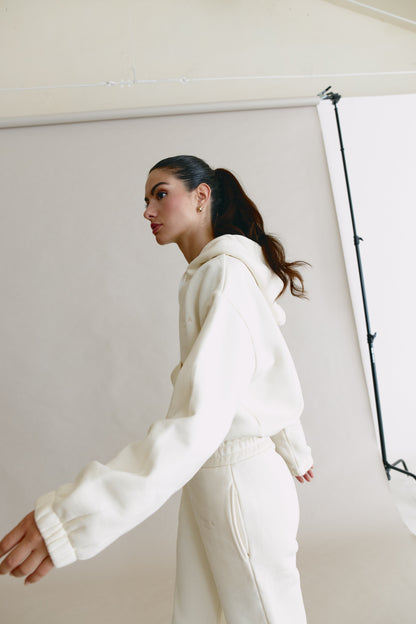 Person wearing a white hoodie and pants in a studio setting